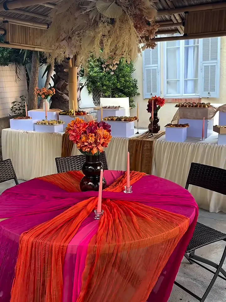 Table ronde drapée de fuchsia et d’orange devant un buffet sous pergola