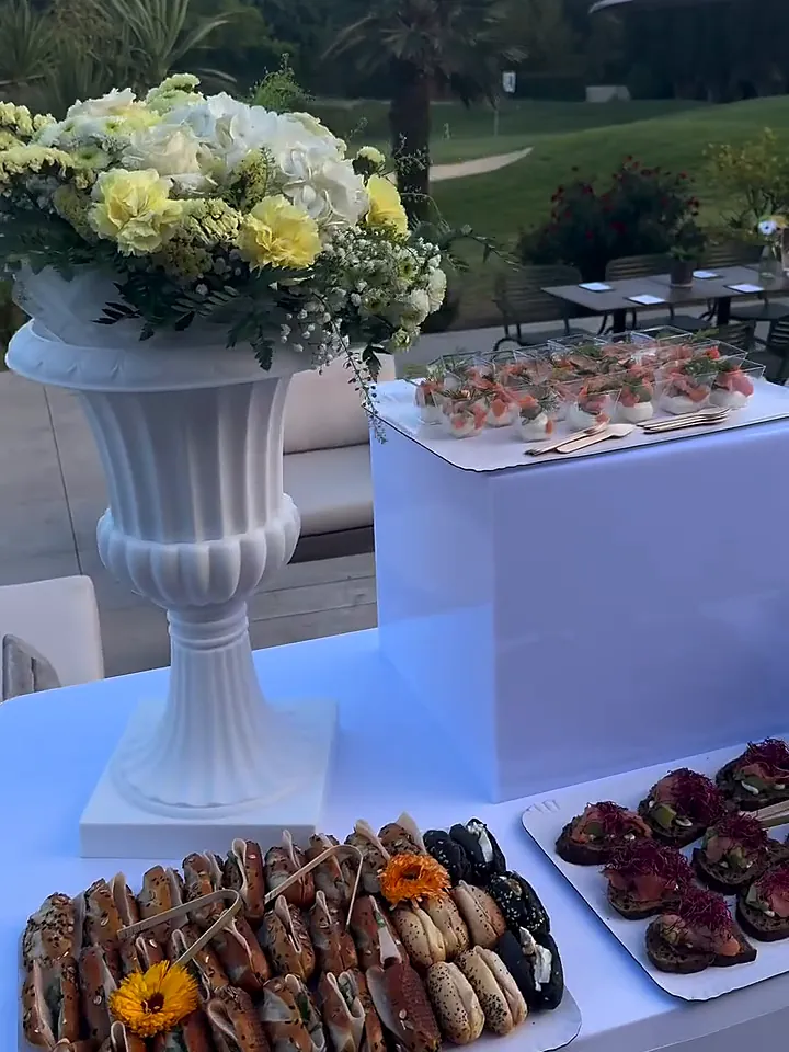 Buffet de fiançailles en terrasse face à un golf, vasque de fleurs jaunes et blanches