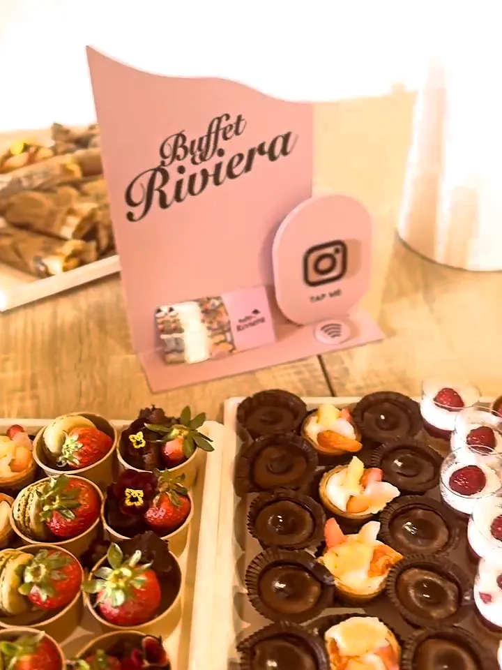 Présentoir rose Buffet Riviera devant des plateaux de tartelettes au chocolat, fraises et macarons